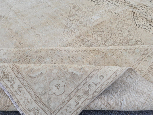 Folded beige and brown Turkish wool rug showing a faded medallion field, floral border and woven reverse