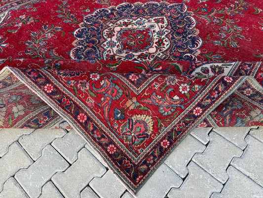 Folded corner of a red Turkish wool rug showing a floral medallion, dark blue border and woven underside