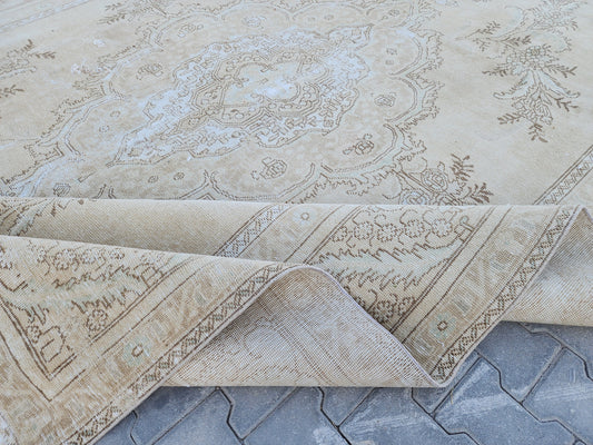 Folded edge of a beige and gray Turkish Oushak wool rug showing its pale central medallion and woven reverse