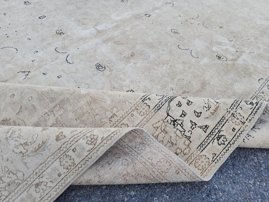 Close view of a pale beige Turkish wool rug with scattered dark motifs, a floral border and folded underside
