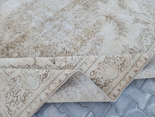 Neutral Turkish Oushak wool rug with a faded medallion and brown scroll motifs, showing folded corners and the underside