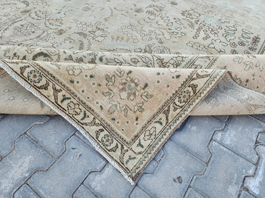 Folded corner of a beige Turkish wool rug with faded brown floral motifs and a narrow patterned border
