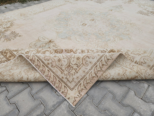 Ivory Turkish wool rug with a faded pale medallion and brown floral border, showing a folded-back corner