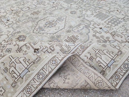 9x13 pale beige vintage wool rug with geometric medallion motifs and a folded corner revealing the woven underside
