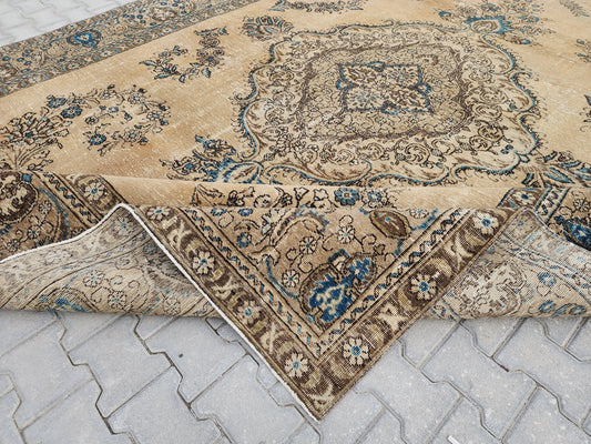Beige Turkish wool rug with a blue and brown floral medallion, showing a folded corner and cotton foundation