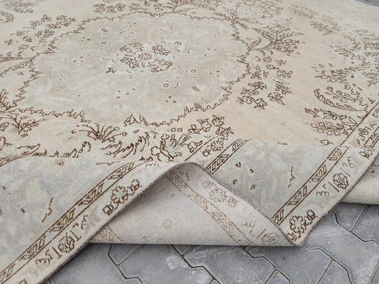 Angled detail of a cream Turkish wool rug with a faded brown medallion and a folded-back corner